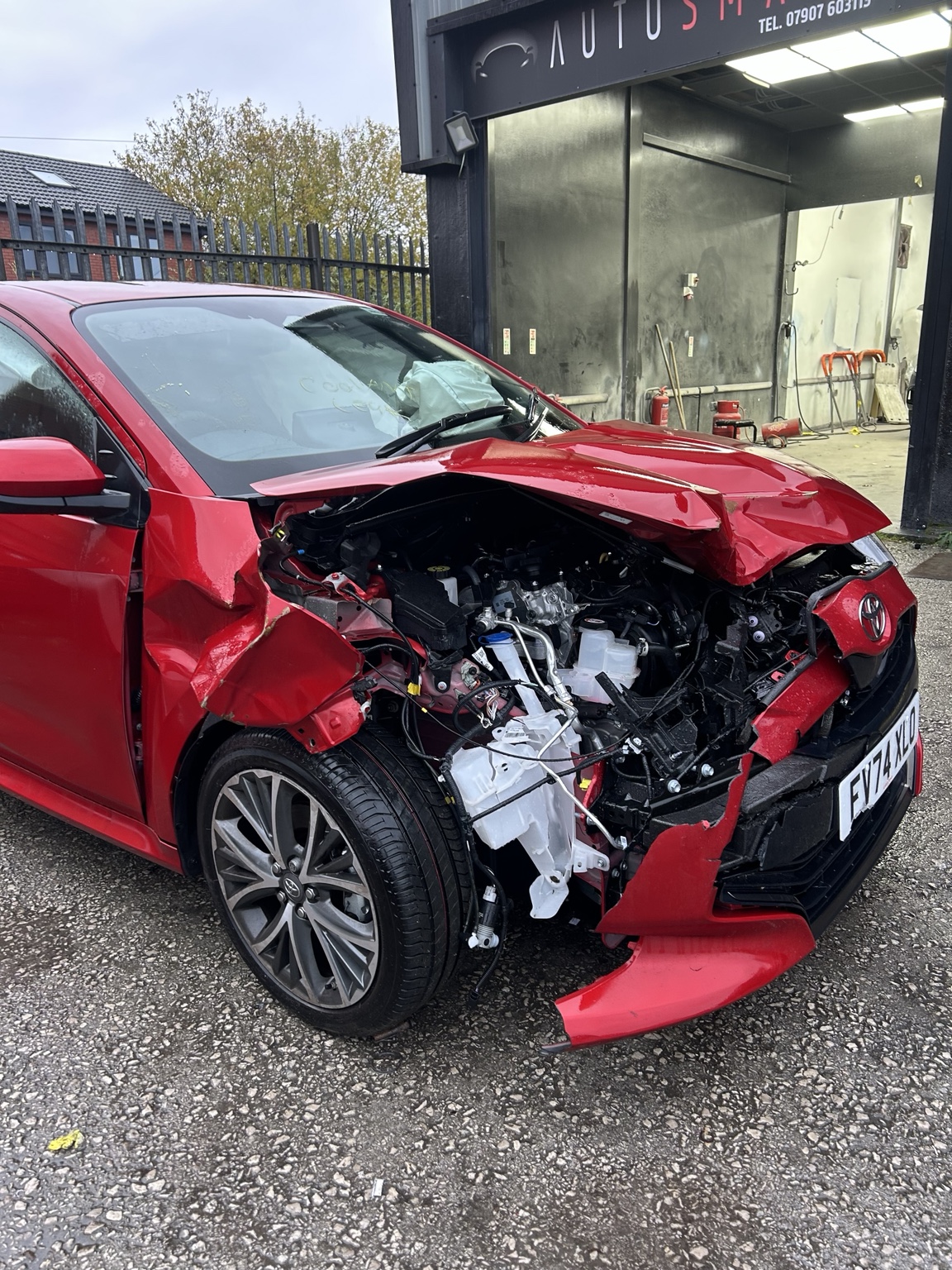 Red vehicle with front-end accident damage outside AutoSmart Body Repair